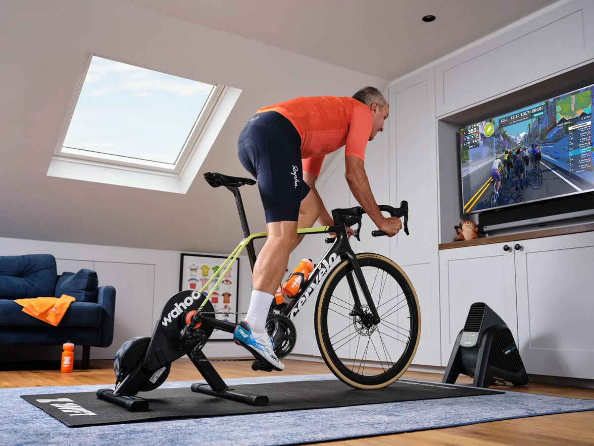 A cyclist riding on a Wahoo smart trainer with Zwift on a large TV in a bright home pain cave